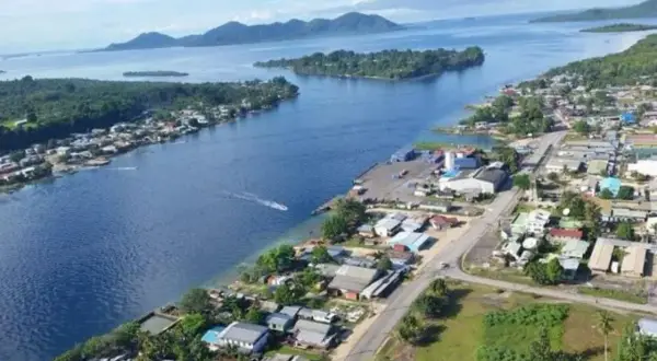 Widok na zatokę z miasteczkiem na wybrzeżu, portem i łodzią. W oddali wyspy i góry. Bougainville.