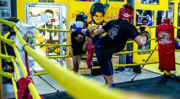 Two fighters practice kicks in a boxing ring, showcasing the intense benefits of sparring for skill development and conditioning.