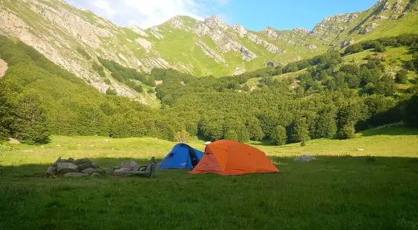 Tende da campeggio in un prato verde, con montagne boscose sullo sfondo, vicino alle sorgenti del Secchia.