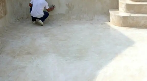 Hombre lijando la pared de una piscina vacía, preparándola para pintar cemento exterior.