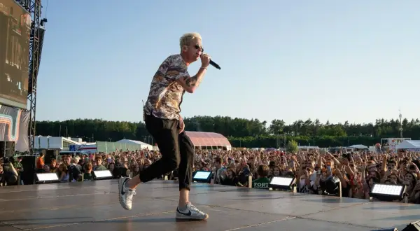 Wokalista One Republic na koncercie, śpiewa do mikrofonu na scenie przed rozentuzjazmowanym tłumem fanów.