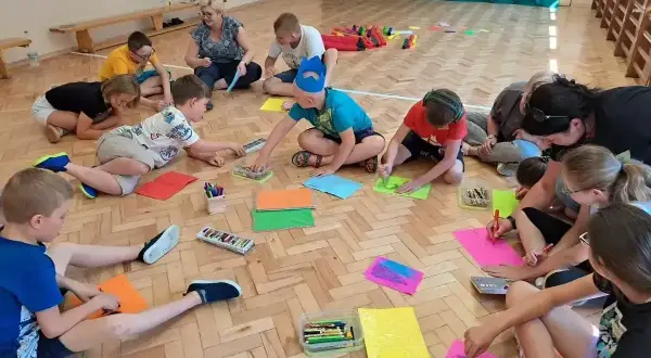 Dzieci klas 1-3 biorą udział w zabawach integracyjnych, rysując i kolorując na podłodze.