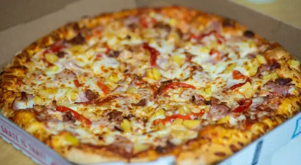 Pyszna pizza hawajska w pudełku, idealna do odgrzania w mikrofali. Ser, szynka i ananas kuszą swoim wyglądem.
