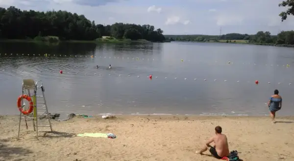 Słoneczny dzień nad rybnikiem zalew. Kąpielisko z bojami, ratownik na posterunku, plażowicze odpoczywają na piasku.
