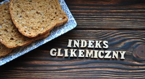 Plasterki chleba pełnoziarnistego na talerzyku z niebieskim wzorem. Obok drewniane litery układają się w napis "INDEKS GLIKEMICZNY".