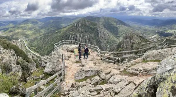 Dos personas admiran el paisaje montañoso desde el mirador del Cerro del Viso. El cielo está nublado.