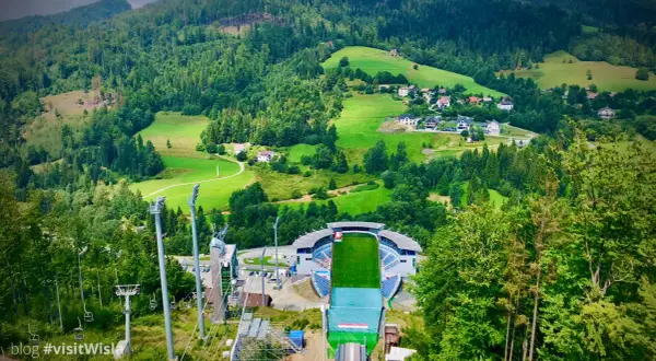 Malownicza panorama Wisły w górach. Widok na skocznię narciarską, wyciągi i zielone wzgórza z domkami.