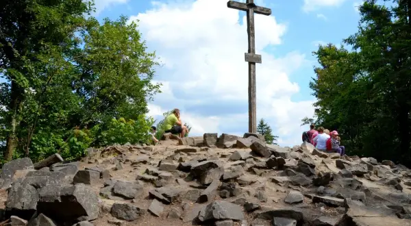 Kamienisty szczyt z drewnianym krzyżem i grupą turystów.