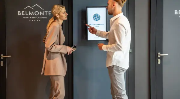 Elegancko ubrana para dyskutuje przy ekranie informacyjnym w hotelu Belmonte.