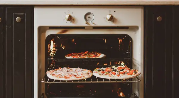 Trois pizzas cuisent dans un four. Le réglage de la température cuisson pizza est visible sur le panneau.
