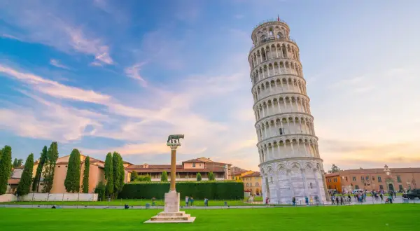 La Torre di Pisa, con il suo fascino inclinato, è al centro di una ricerca visiva, circondata da un prato verde e un cielo al tramonto.