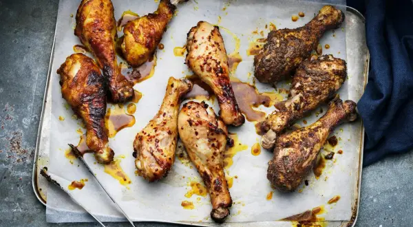 Nio saftiga kycklingben, vissa kryddade med chili, ligger på en plåt. Perfekt innertemp kycklingben för en härlig måltid.