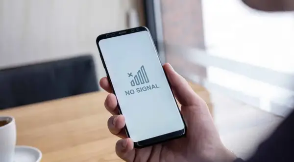 Dłoń trzyma smartfon z komunikatem "NO SIGNAL". Brak sieci w telefonie uniemożliwia kontakt.