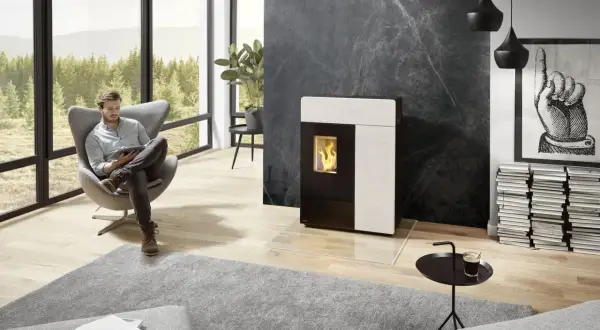 Un homme lit dans un fauteuil près d'un poêle moderne. Le **carrelage derrière le poêle** en marbre noir crée un contraste saisissant.
