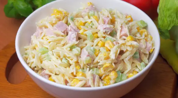 Pyszna sałatka z makaronem orzo, kukurydzą, szynką i selerem, polana kremowym sosem.