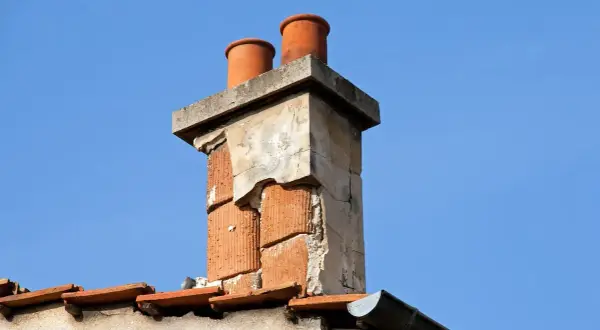 Zwei Ziegelrohre ragen aus einem alten, beschädigten Schornstein. Der **Schornstein nass unten** zeigt deutliche Verwitterungsspuren.