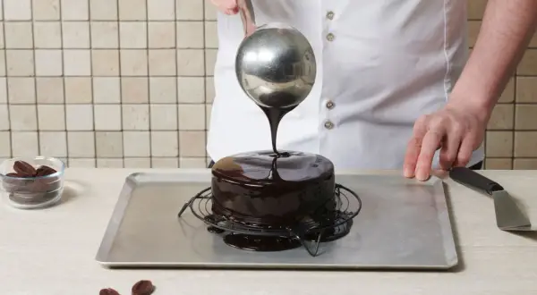 Un chef verse un glaçage miroir brillant sur un gâteau au chocolat.