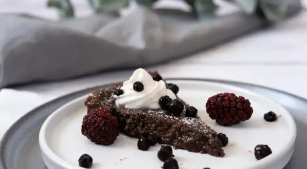 En bit vegansk kladdkaka med vispgrädde och bär.