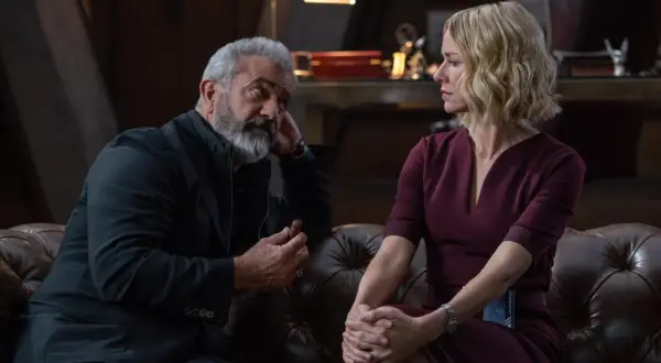 Mel Gibson w filmie, z cygarem w dłoni, rozmawia z kobietą w bordowej sukience.
