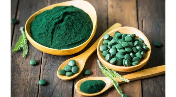 Chlorella vs spirulina: zielony proszek i tabletki na drewnianym tle. Dwa rodzaje alg w formie suplementów diety.