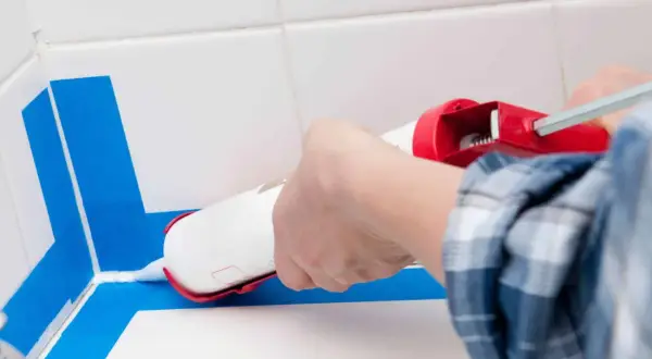 Application d'un joint époxy pour douche, avec du ruban bleu pour un résultat net.
