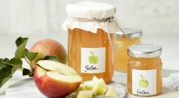 Zwei Gläser mit selbstgemachtem Apfelgelee, daneben frische Äpfel und gewürfelte Apfelstücke. Ein leckeres Apfelgelee Rezept zum Nachmachen.