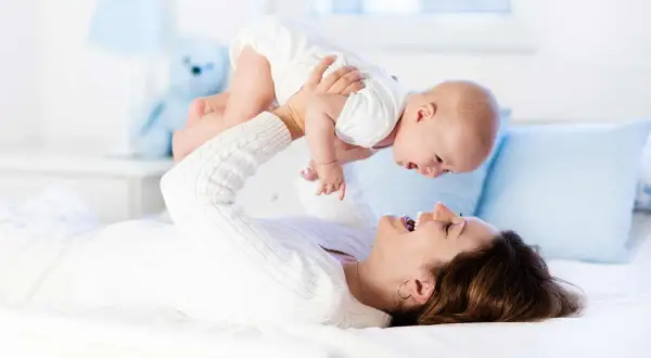 Szczęśliwa mama podrzuca dziecko, zastanawiając się, ile kosztuje opieka nad dzieckiem za godzinę.