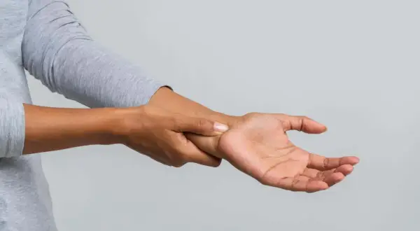 Eine Person hält sich das Handgelenk, als ob sie ein Ziehen im Handgelenk spürt.