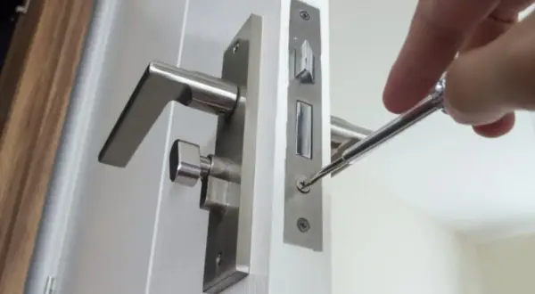 Réparation d'une poignée de porte qui claque avec le vent. Un tournevis ajuste la serrure.