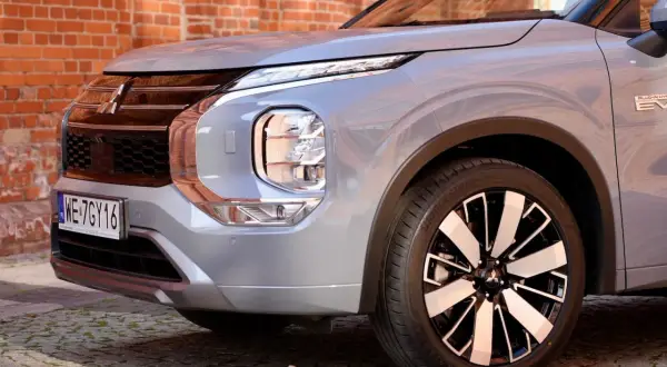 Przód srebrnego Mitsubishi Outlander 2025 z charakterystycznym grillem i reflektorami LED, zaparkowany na bruku przed ceglaną ścianą.