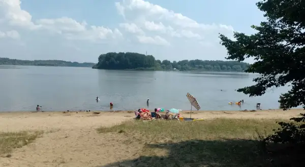 Słoneczny dzień nad jeziorem przeczyckim. Ludzie odpoczywają na plaży i kąpią się w wodzie.