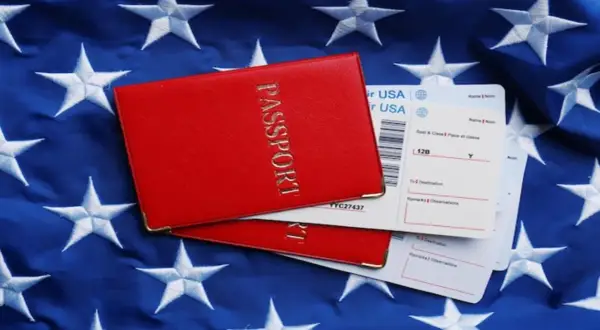 Czerwony paszport i bilety lotnicze na tle flagi USA. Zastanawiasz się, ile kosztuje bilet do USA w dwie strony?