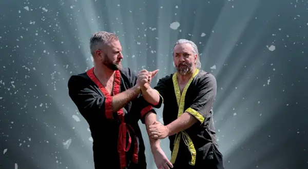 Två män i traditionella dräkter tränar wing chun. Ljuset strålar bakom dem.