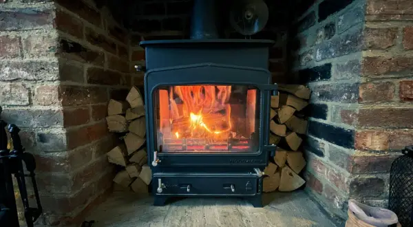 Poêle à bois allumé dans une cheminée en briques, avec du bois empilé. La **réglementation tubage poêle à bois** assure une évacuation sûre des fumées.