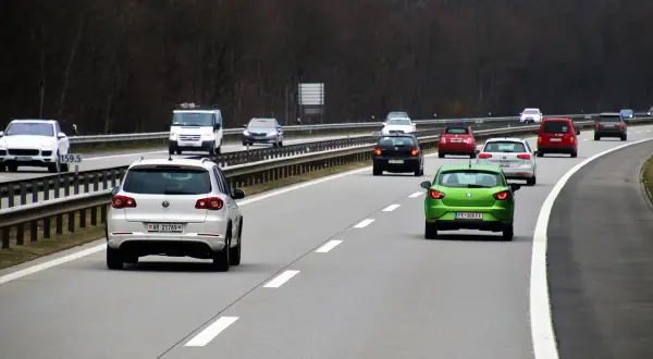 Samochody poruszają się po autostradzie, każdy na swoim pasie ruchu. Zielony samochód z przodu wyznacza tempo.
