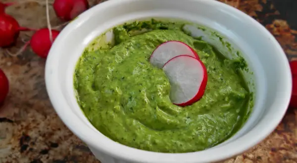 Zielone pesto z liści rzodkiewki w białej miseczce, ozdobione plasterkami rzodkiewki.