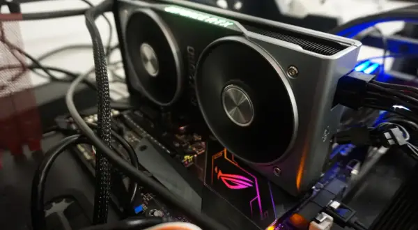 Karta graficzna RTX 2060 z zielonym podświetleniem "GeForce RTX" i wentylatorami. Widać jej dużą ilość vram, podłączoną do płyty głównej z podświetlanym logo ROG.