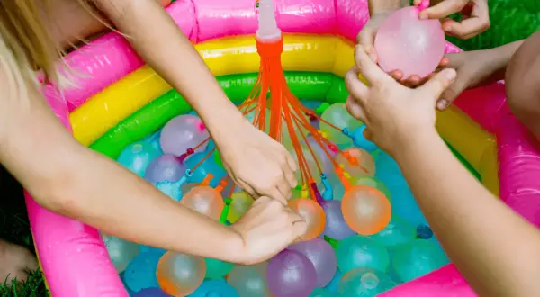 Manos infantiles llenando globos de agua en una piscina inflable multicolor. ¡Diversión garantizada con estos juegos de agua!