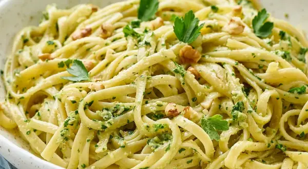 Pasta con pesto cremosa, adornada con nueces y perejil fresco. Un plato italiano delicioso y vibrante.