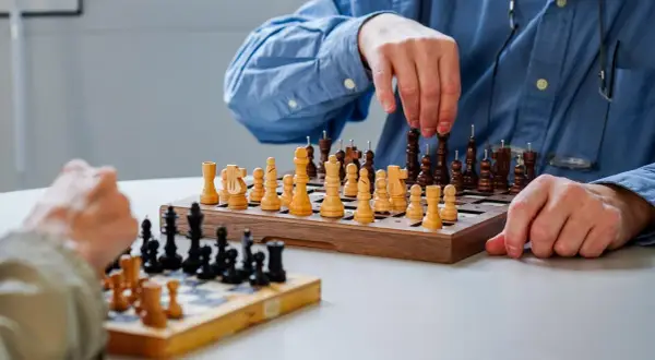 Deux personnes jouent aux échecs. Les pièces ont des ergots pour aider à les identifier, rendant ce jeu accessible aux aveugles.