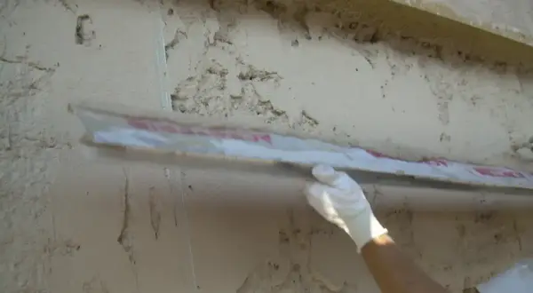 Applicazione di intonaco traspirante su una parete grezza con una spatola. La finitura garantisce la salute dell'edificio.