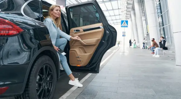 Kobieta wysiada z luksusowego SUV-a, trzymając dokumenty, które mogą być związane z umową użyczenia samochodu.