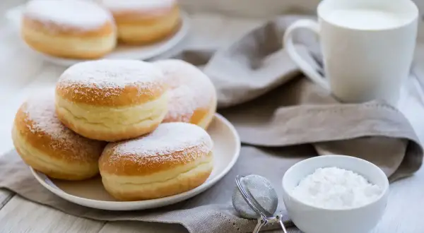 Bomboloni alla crema spolverati di zucchero a velo, pronti per essere gustati con una tazza di latte.
