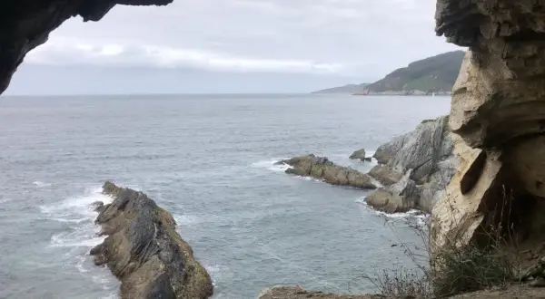 Vista desde la cova da doncela. El mar agitado choca contra las rocas mientras una vela solitaria navega en el horizonte.