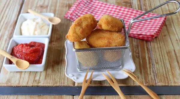 Croquetas de gambas doradas y crujientes en una cesta metálica, acompañadas de ketchup y mayonesa.