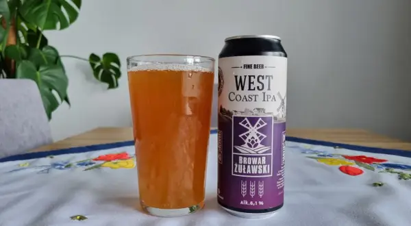 Szklanka piwa West Coast IPA obok puszki Browaru Żuławski. Na obrusie haftowane kwiaty.