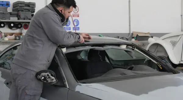 Taller mecánico. Un hombre trabaja en el techo de un coche gris, solucionando stage 1 problemas.