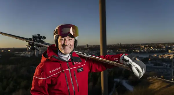 Ski-entusiast med skidor på axeln, klädd i röd jacka med SkiStar-logga. Han ser ut att vara en del av SkiStar ledning, redo för äventyr.
