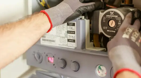 Ręce w rękawiczkach pracują przy budowie bojlera elektrycznego, regulując pompę Grundfos.
