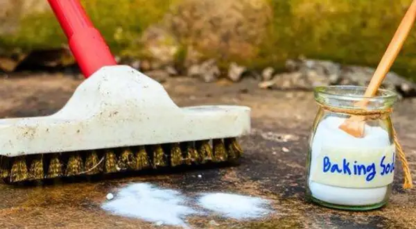 Brosse et bicarbonate de soude prêts pour nettoyer une terrasse en pierre.